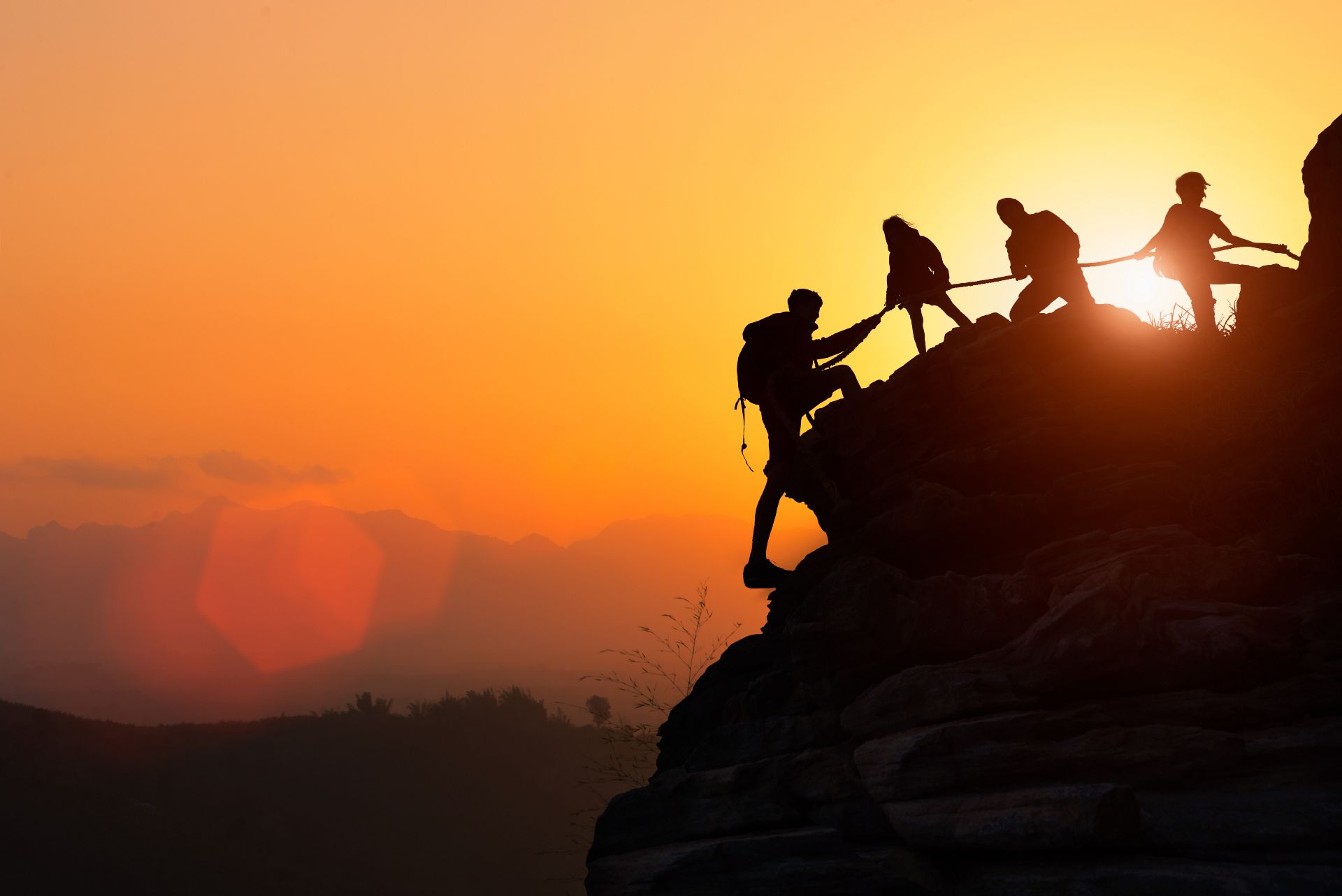 People climbing a rock together with a rope at sunset