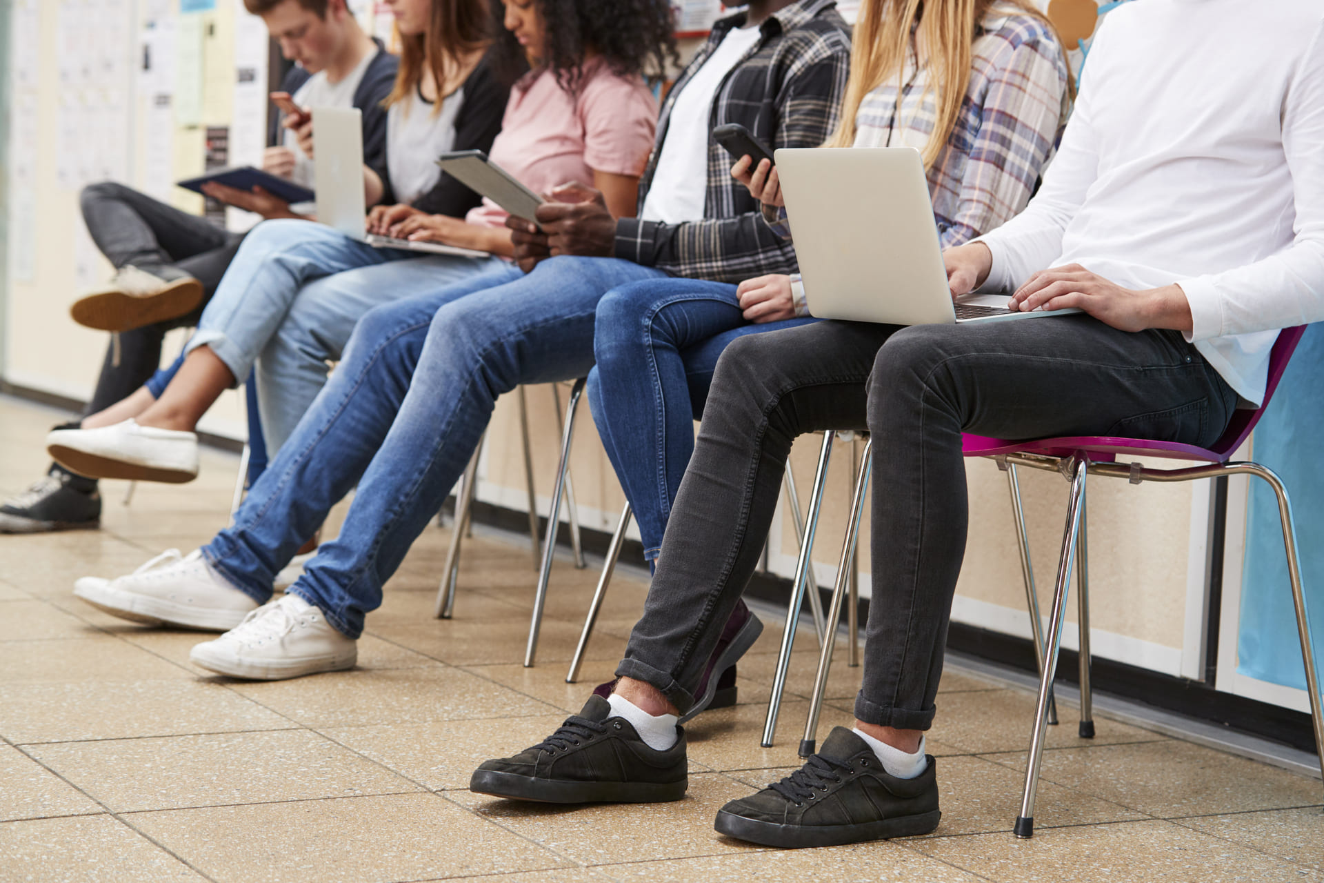 Young people sitting on chairs looking at laptops and phones