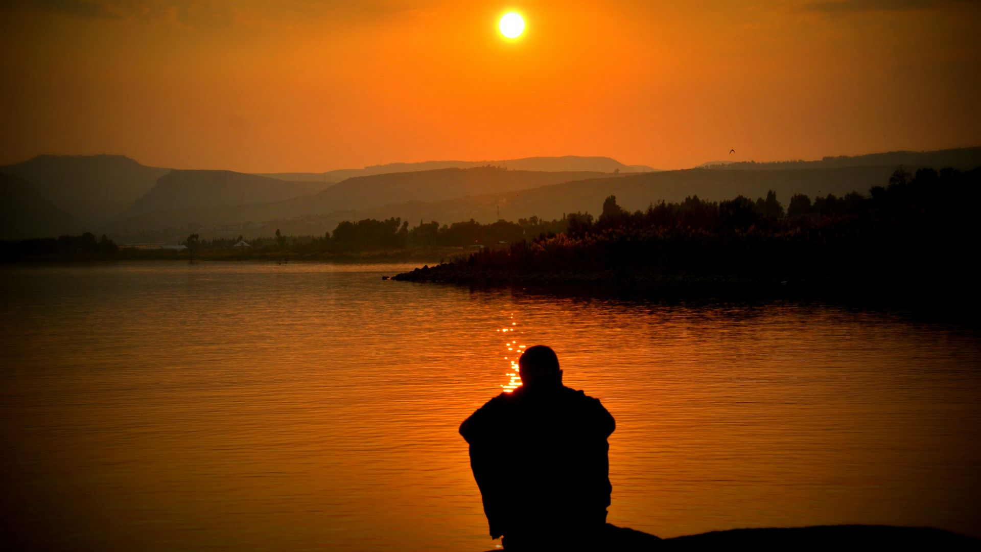 Person sitting by lake at sunset